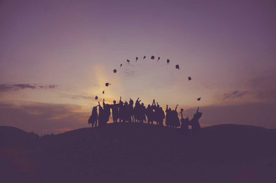 Graduating students throw caps in the air at sunset.